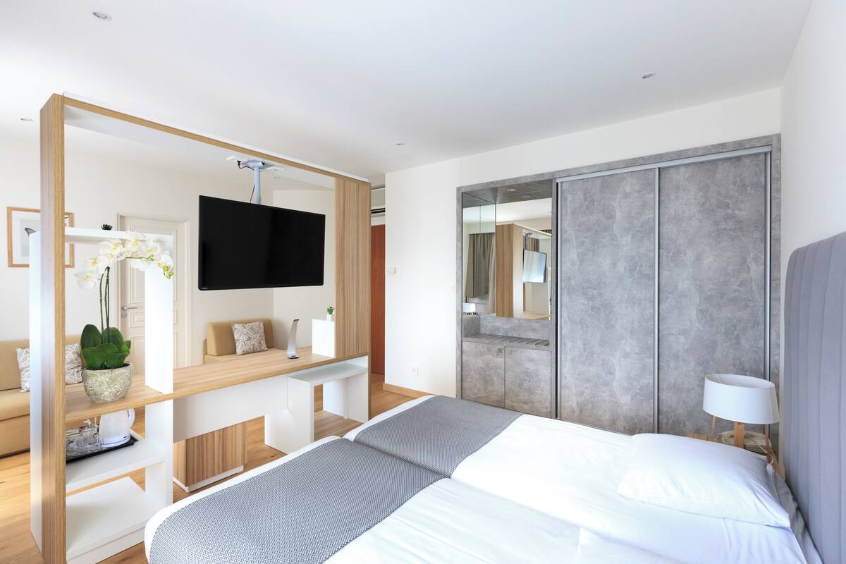 A modern hotel room with a bed, a TV, a desk, and a large mirror.