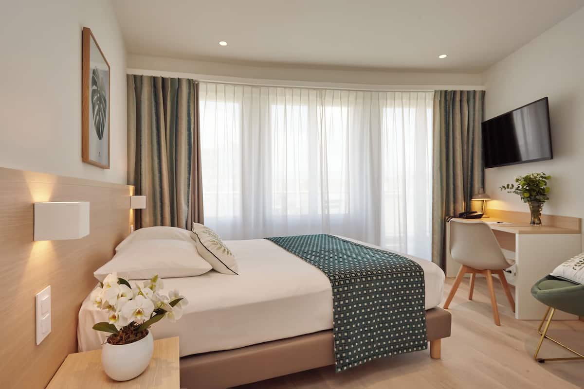 A hotel room with a bed, bedside table, desk, chair, TV, and curtains.
