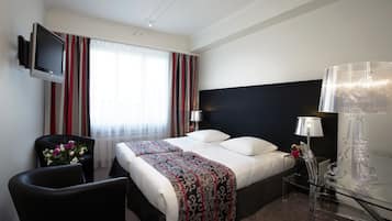Habitación de hotel con una cama, televisor montado en la pared, escritorio con lámpara y una silla.