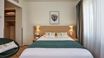 Una habitación de hotel con una cama, una silla, una mesita de noche, un cuadro colgado en la pared y una ventana con cortinas.