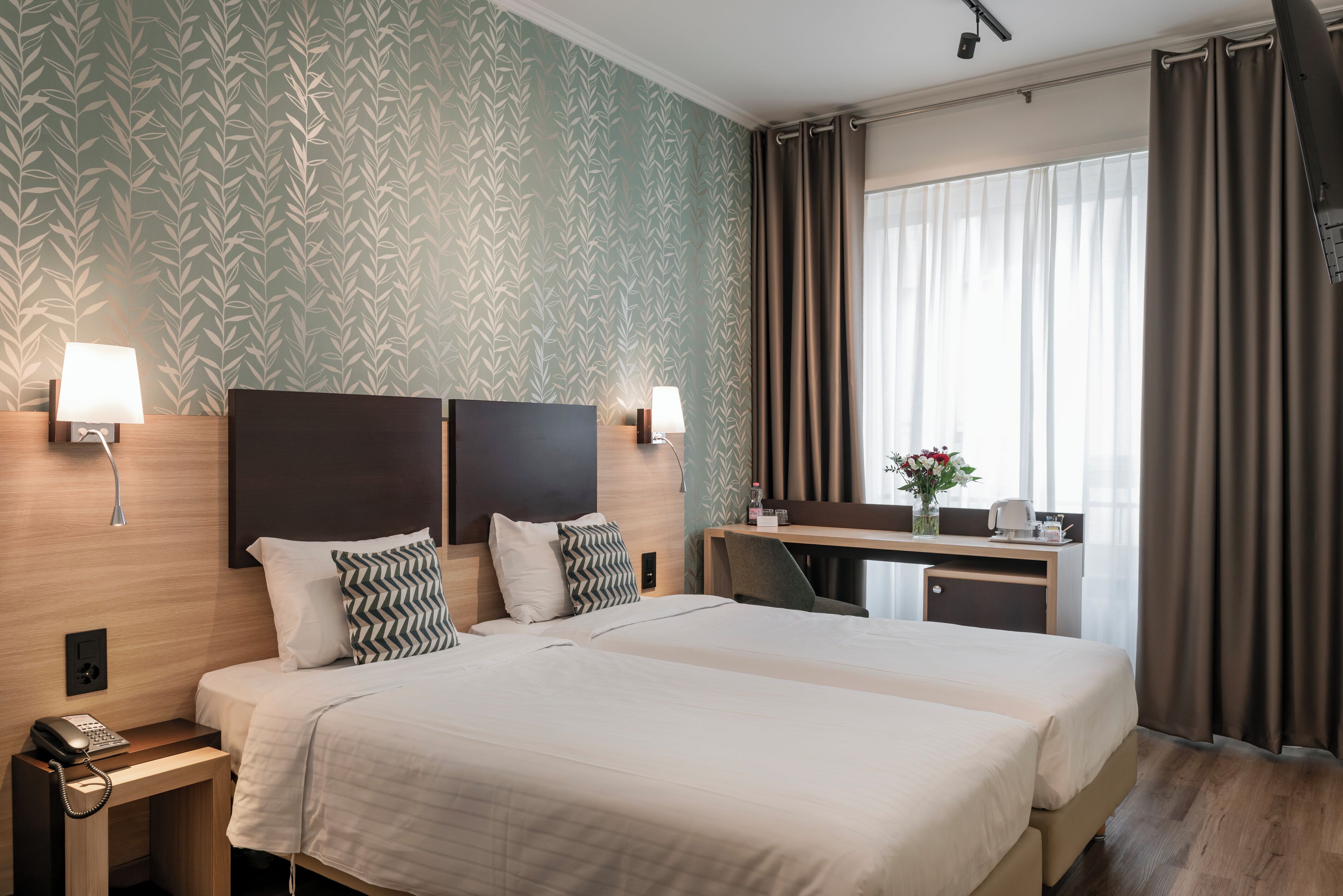 A hotel room with two beds, a desk, a chair, a telephone, and a window with curtains.