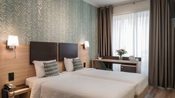 A hotel room with two beds, a desk, a chair, a telephone, and a window with curtains.