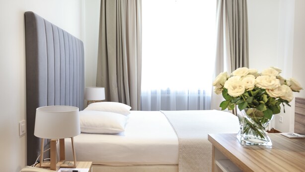 A neatly made bed with a white comforter and pillows, a bedside lamp, a telephone, and a vase with white flowers on a wooden nightstand. - Hotel Suisse (Geneva)