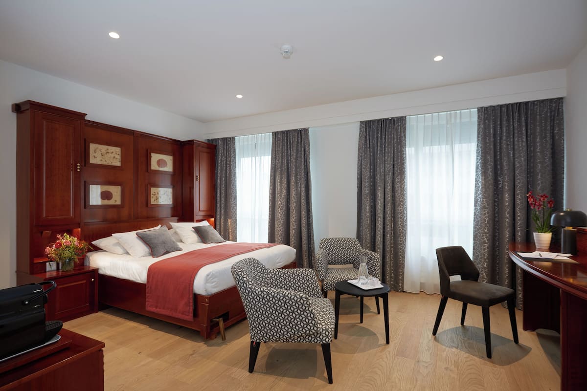 A hotel room with a large bed, two armchairs, a desk, and a small table.