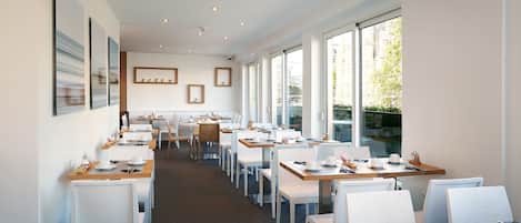 A modern dining area with multiple tables and chairs, large windows offering views of the city, and a clean, minimalist decor.