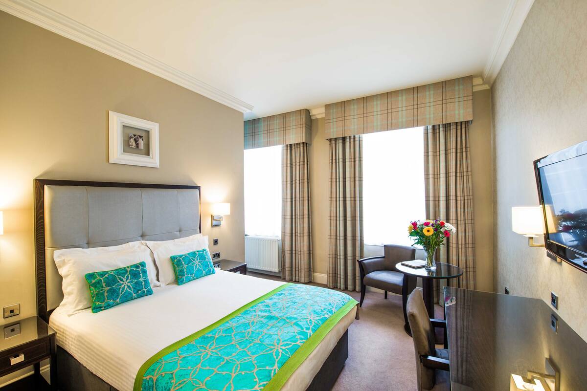 A hotel room with a large bed, a desk with a chair, a TV, and a window with curtains.