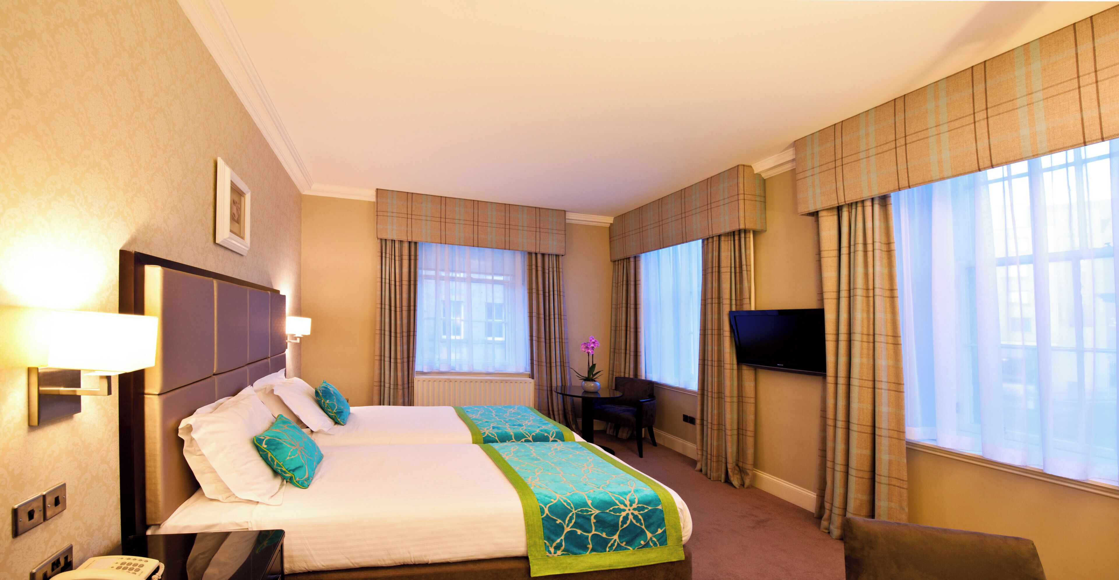 A hotel room with two beds, a desk, a chair, a television, and a window with curtains.