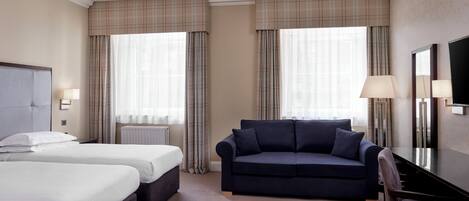Een hotelkamer met twee bedden, een donkerblauwe bank, een bureau en een grote spiegel.