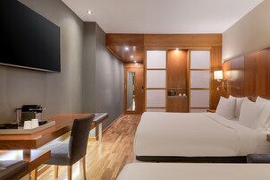 Ein modernes Hotelzimmer mit einem großen Bett, einem Schreibtisch mit Stuhl, einem Flachbildfernseher und einer Wandpaneele aus Holz.