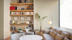 Una sala de estar moderna con una mesa redonda de mármol, un sofá color beige y una estantería llena de libros y objetos decorativos.