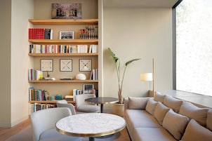 Ein modernes Wohnzimmer mit einem runden Marmortisch, einem beigen Sofa und einer Bücherwand mit Büchern und Dekoration.