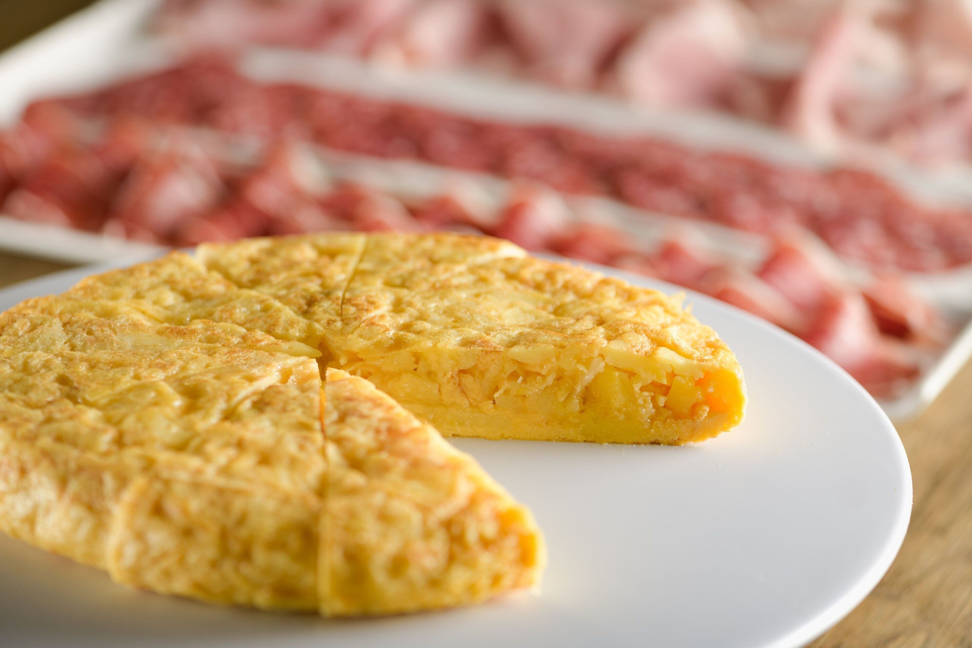A slice of omelette on a white plate with a blurred background of meat.