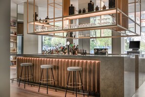 Un área de bar moderna con mostrador de madera, varios taburetes y estantes con botellas y copas.