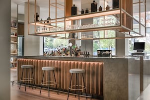 Eine moderne Bar mit einer Holztresen, mehreren Hockern und Regalen mit Flaschen und Gläsern.