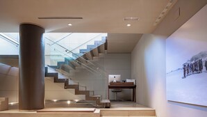 Un interior moderno con una escalera que conduce a un nivel superior, un escritorio con computadora y una proyección montada en la pared.