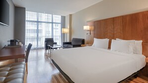 Habitación de hotel con una cama grande, un escritorio con una silla, un sofá y un televisor montado en la pared.