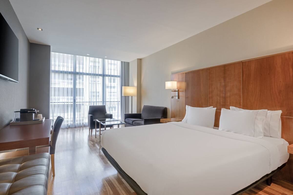 Une chambre d’hôtel avec un grand lit, un bureau avec une chaise, un canapé et un téléviseur fixé au mur.