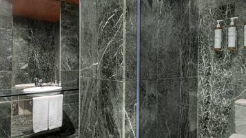 A modern bathroom with a glass-enclosed sink, marble walls, and toiletries on a wall-mounted dispenser.