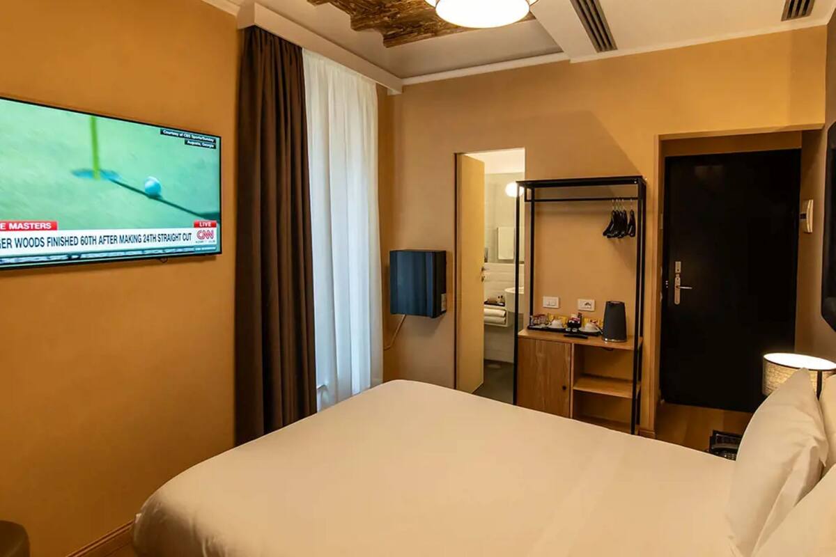 A hotel room with a bed, a TV displaying a golf game, a mirror, a wardrobe, and a door.