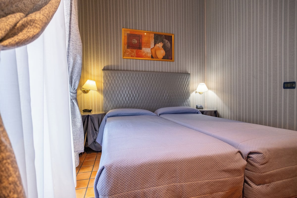 Un letto matrimoniale con testiera imbottita, due lampade ai comodini e un quadro sopra il letto.
