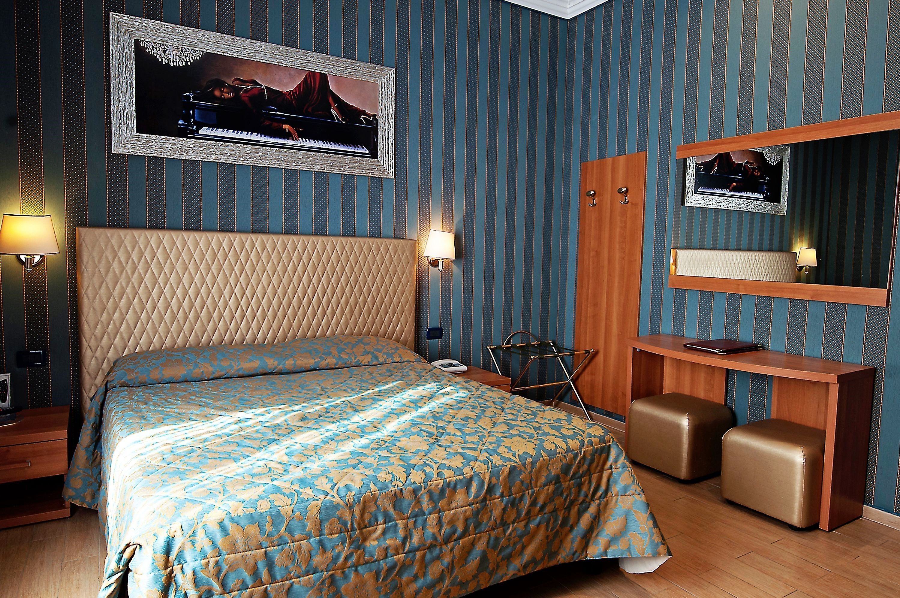 A bedroom with a large bed, a wooden desk, a mirror, and a piano.