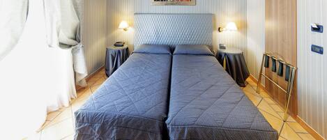 A double bed with a quilted headboard, two bedside tables with lamps, a wooden wardrobe, and a framed picture on the wall.