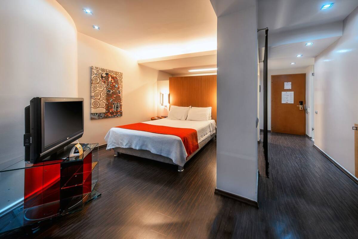 Ein Hotelzimmer mit Bett, Fernseher, einem roten Schrank und einer Holztür.