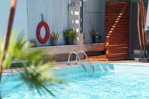 Piscina com deck de madeira, plantas em vasos e boia salva-vidas.