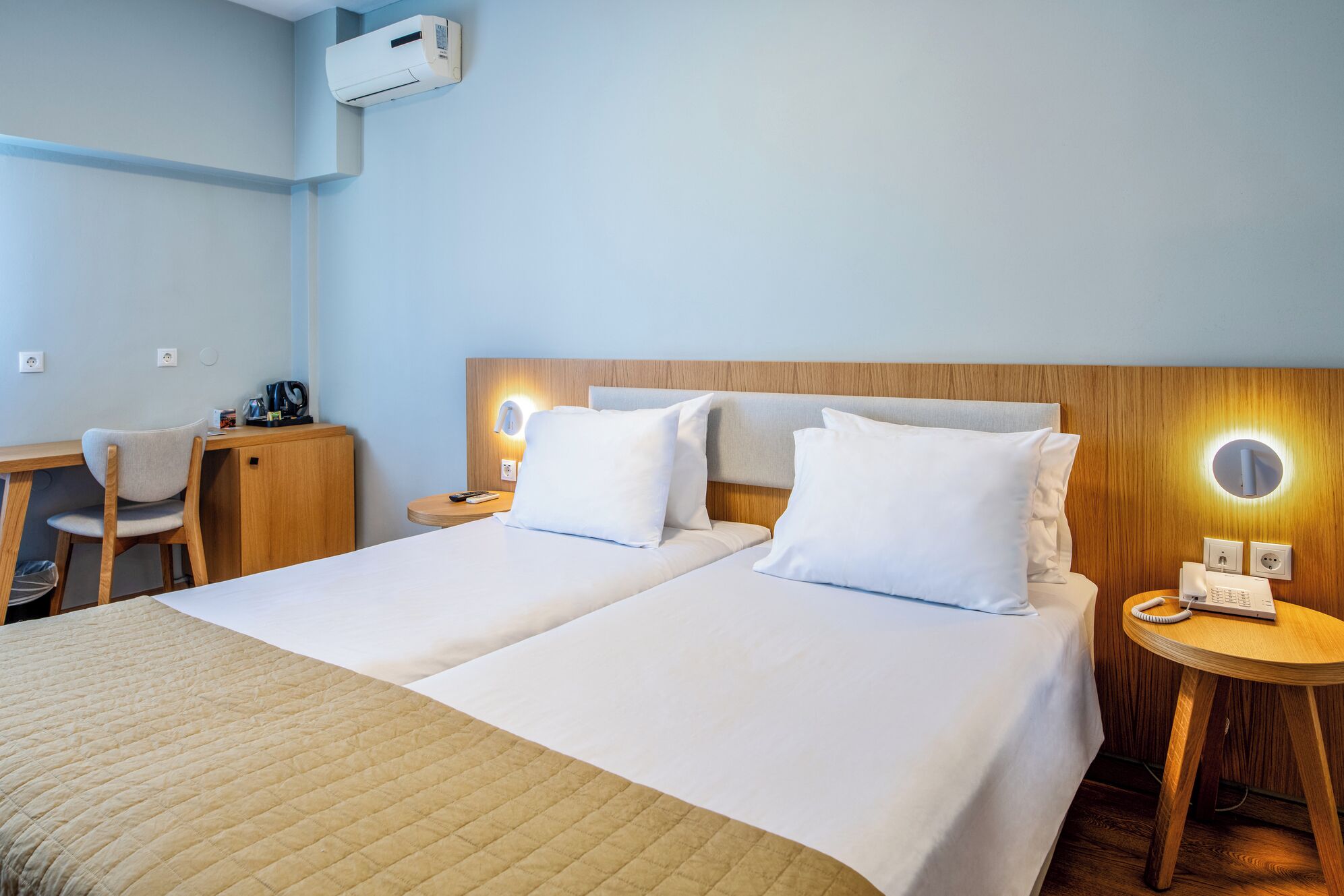 Habitación de hotel con dos camas, un escritorio, una silla, una mesita de noche con teléfono y aire acondicionado instalado en la pared.