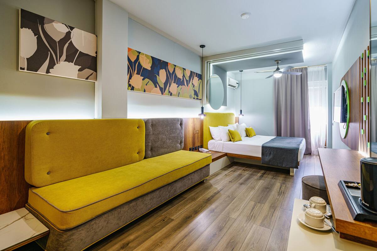 Ein modernes Hotelzimmer mit einer Couch, einem Bett, einem Nachttisch und einem großen Spiegel.
