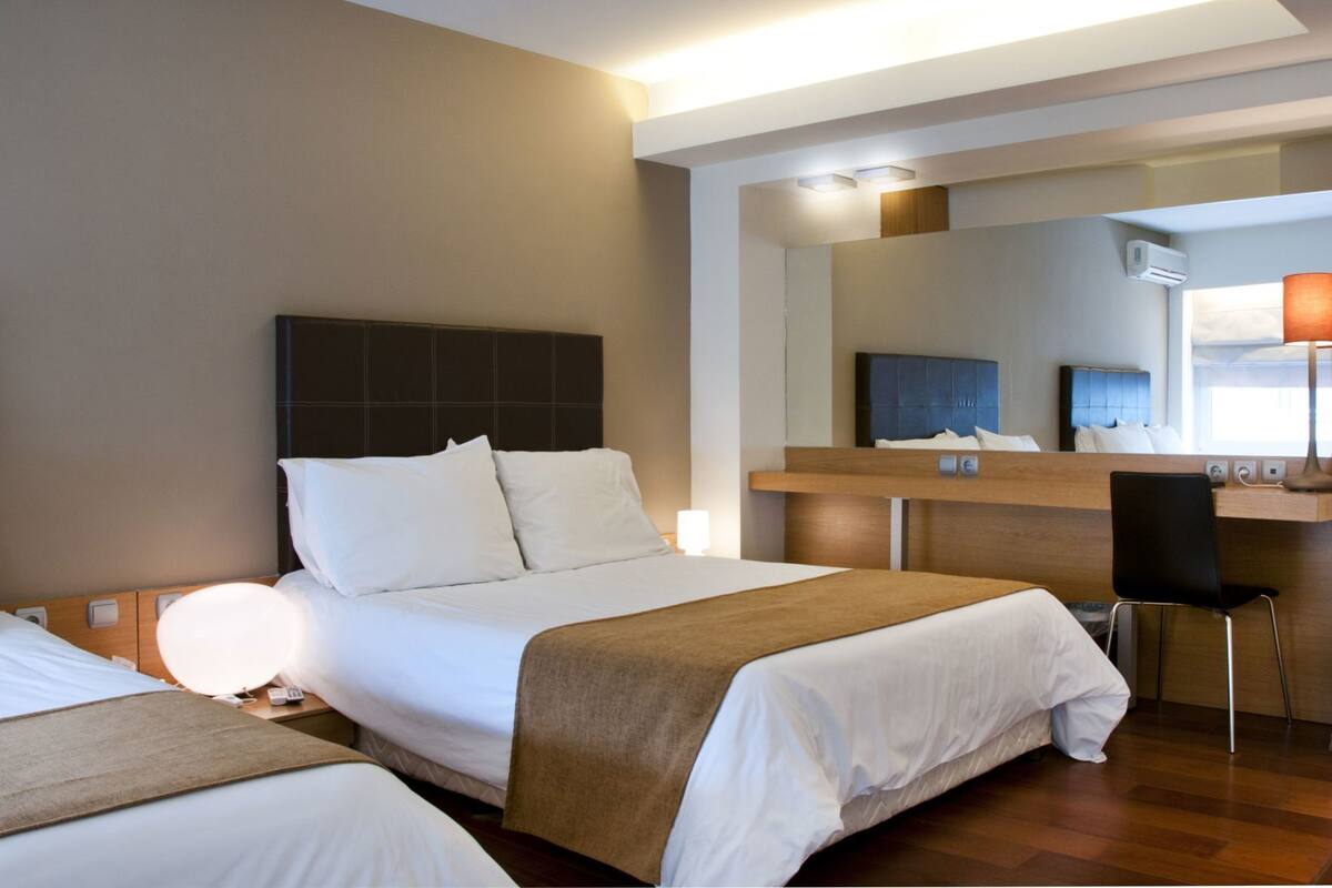 Ein Hotelzimmer mit Bett, Nachttisch, Lampe, Stuhl und Schreibtisch mit Spiegel.