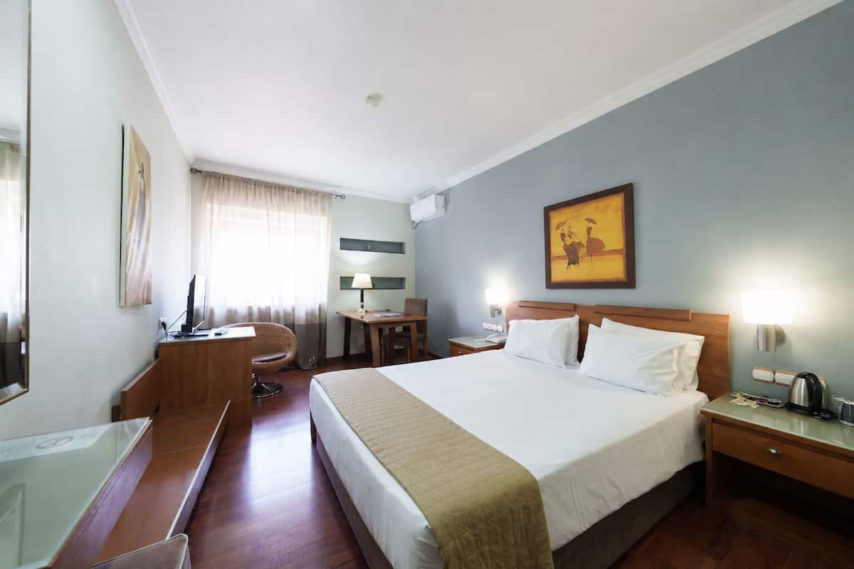 Ein Hotelzimmer mit Bett, Schreibtisch, Stuhl, Nachttisch, Lampe und Kunstwerk.