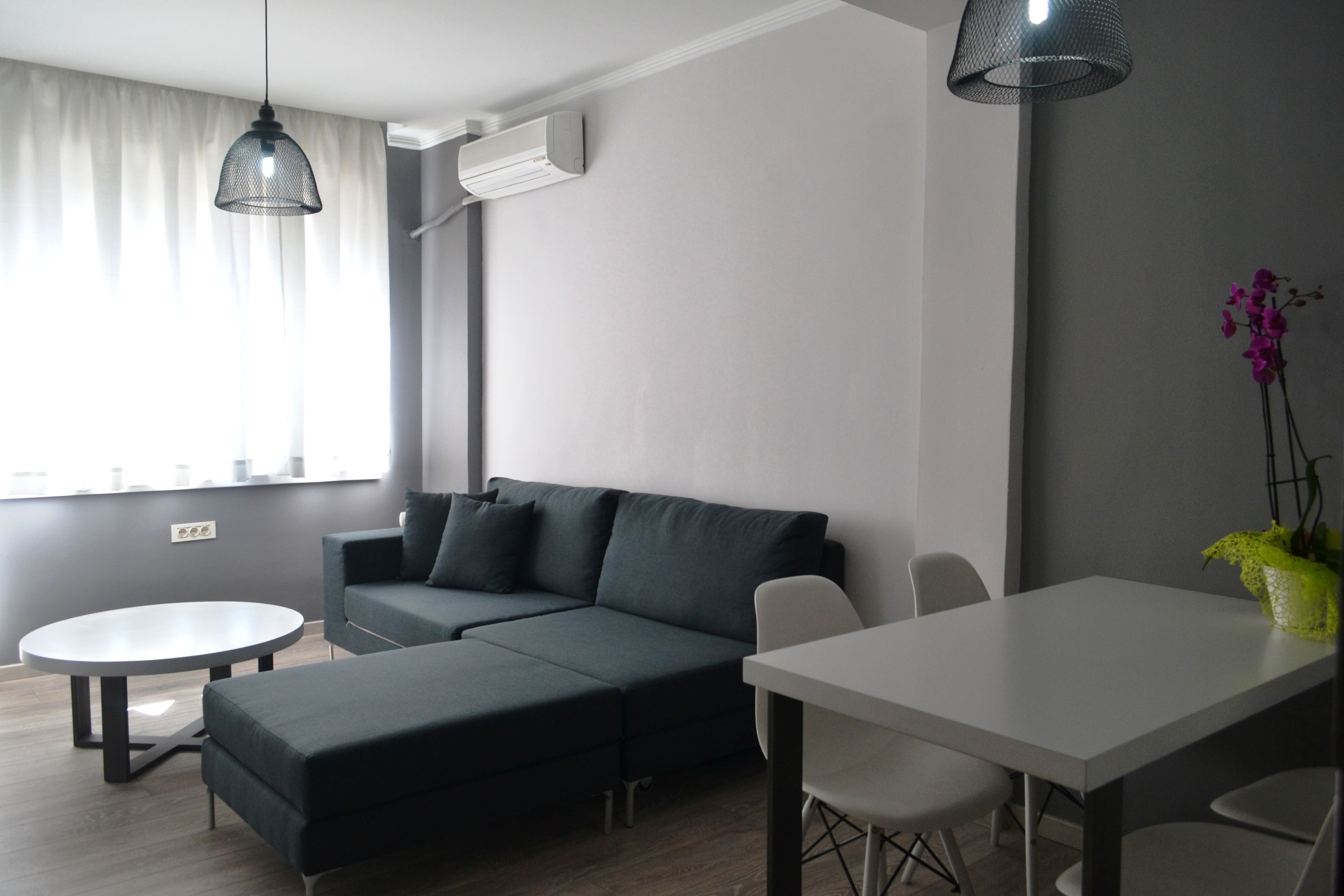 Una sala moderna con un sofá modular, una mesa de comedor redonda y una pequeña mesa blanca.
