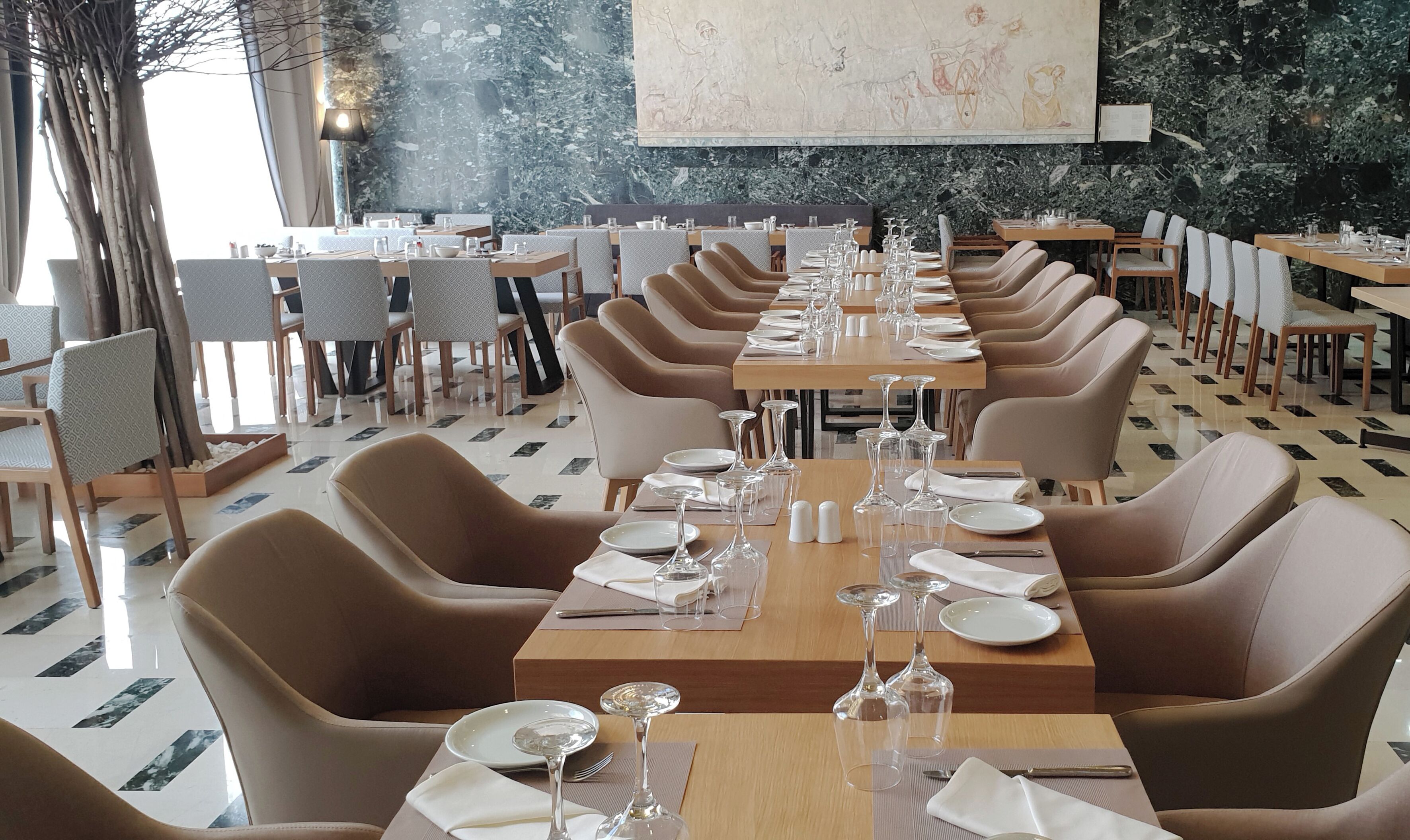 A restaurant with long tables, chairs, and a large mural on the wall.