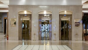 A spacious lobby with a large chandelier, three elevators, and a patterned floor. - Capsis Hotel Thessaloniki (Thessaloniki)