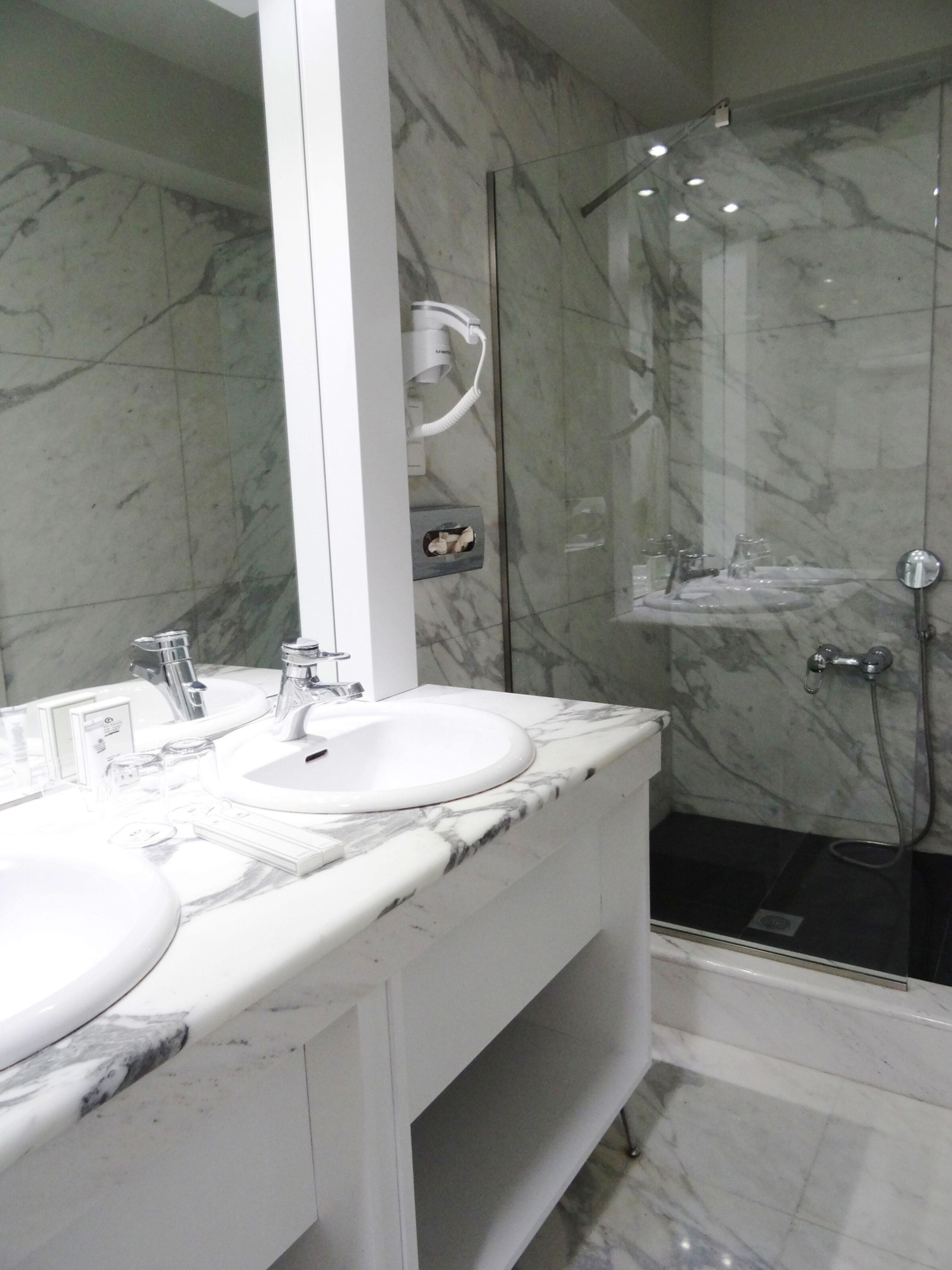 Une salle de bain avec deux lavabos, un grand miroir et une douche séparée par une paroi de verre.