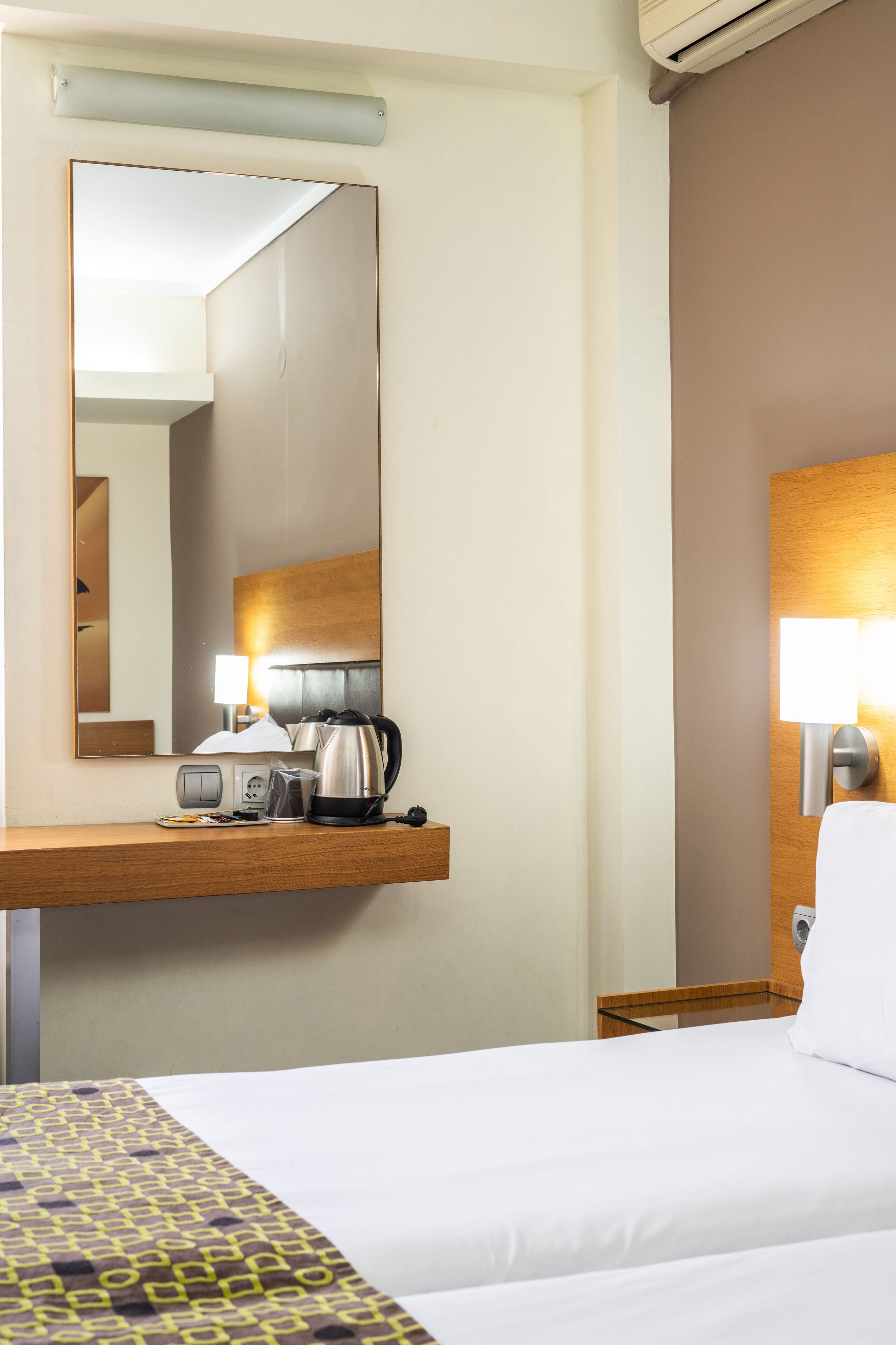 Una camera d'albergo con un letto, un comodino, uno specchio, una lampada e una macchina per il caffè.