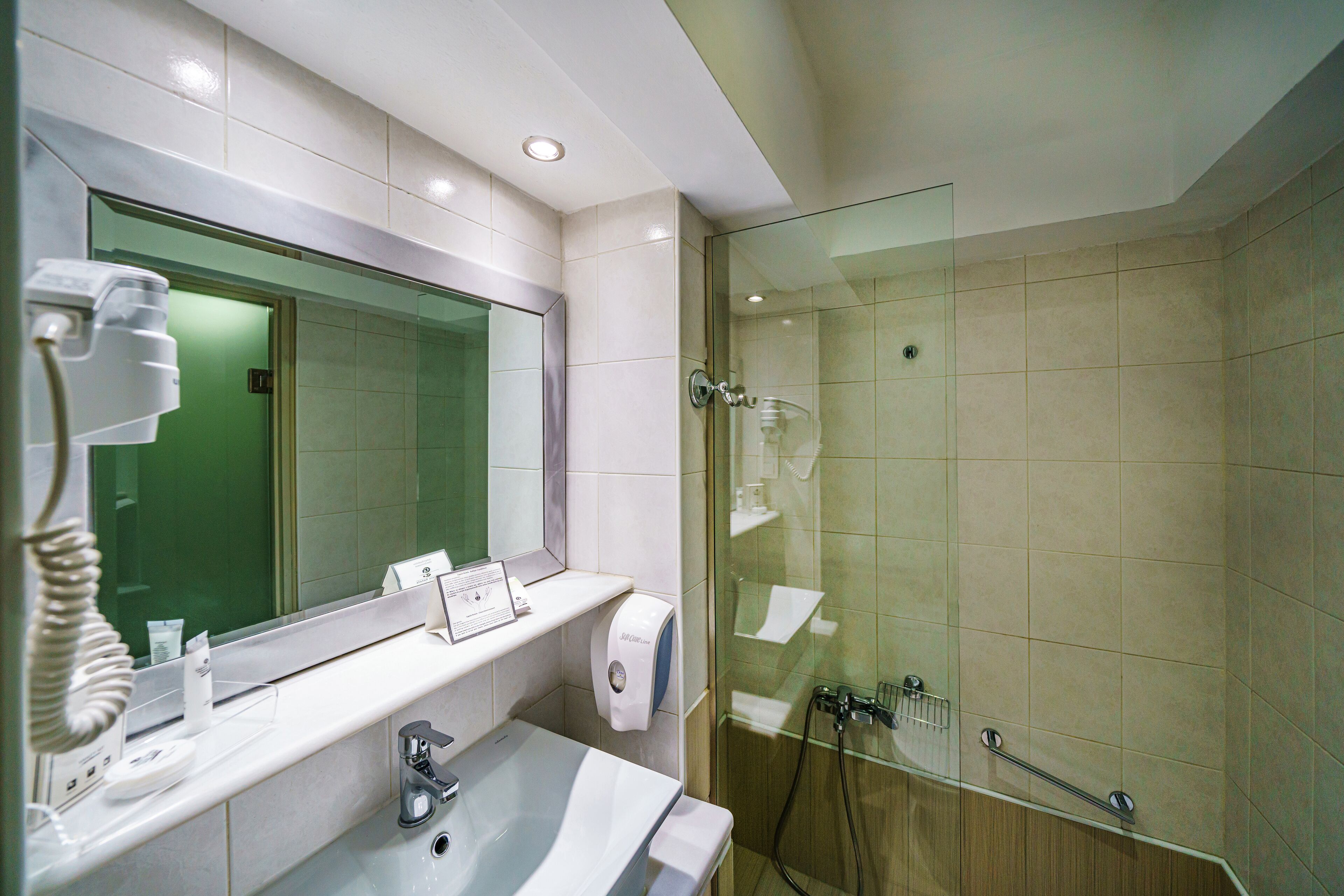 Un baño moderno con un espejo grande, un lavamanos, una ducha con cerramiento de vidrio y un secamanos.