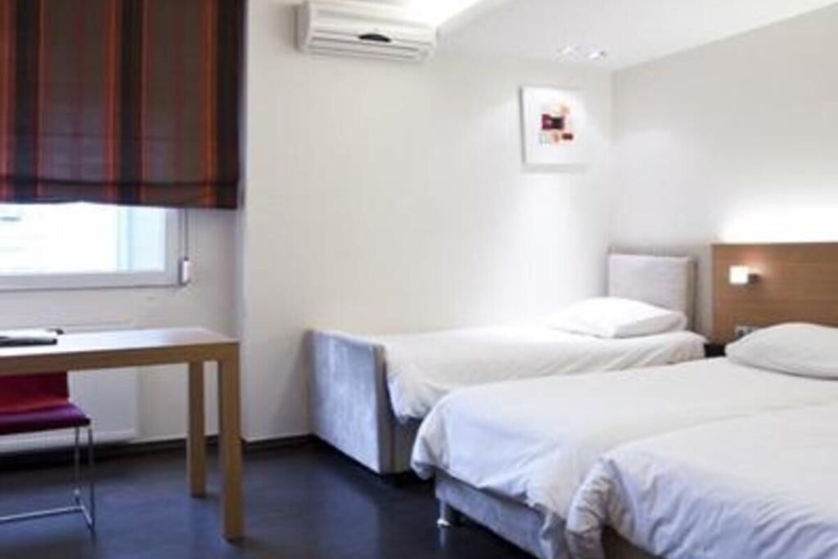 A hotel room with two beds, a desk, and a window with curtains.
