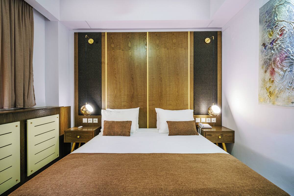Ein Hotelzimmer mit einem großen Bett, zwei Nachttischen mit Lampen, einem Holzkopfteil und einem Bild an der Wand.