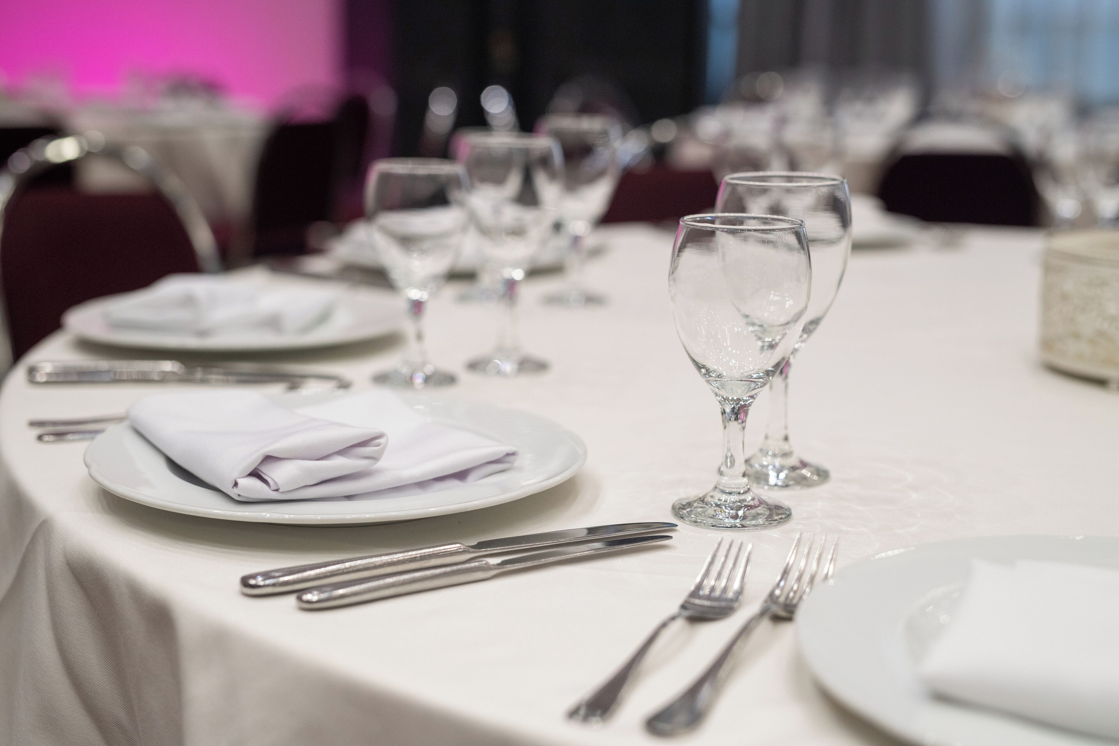 A dining table set with white tablecloth, plates, cutlery, and wine glasses.