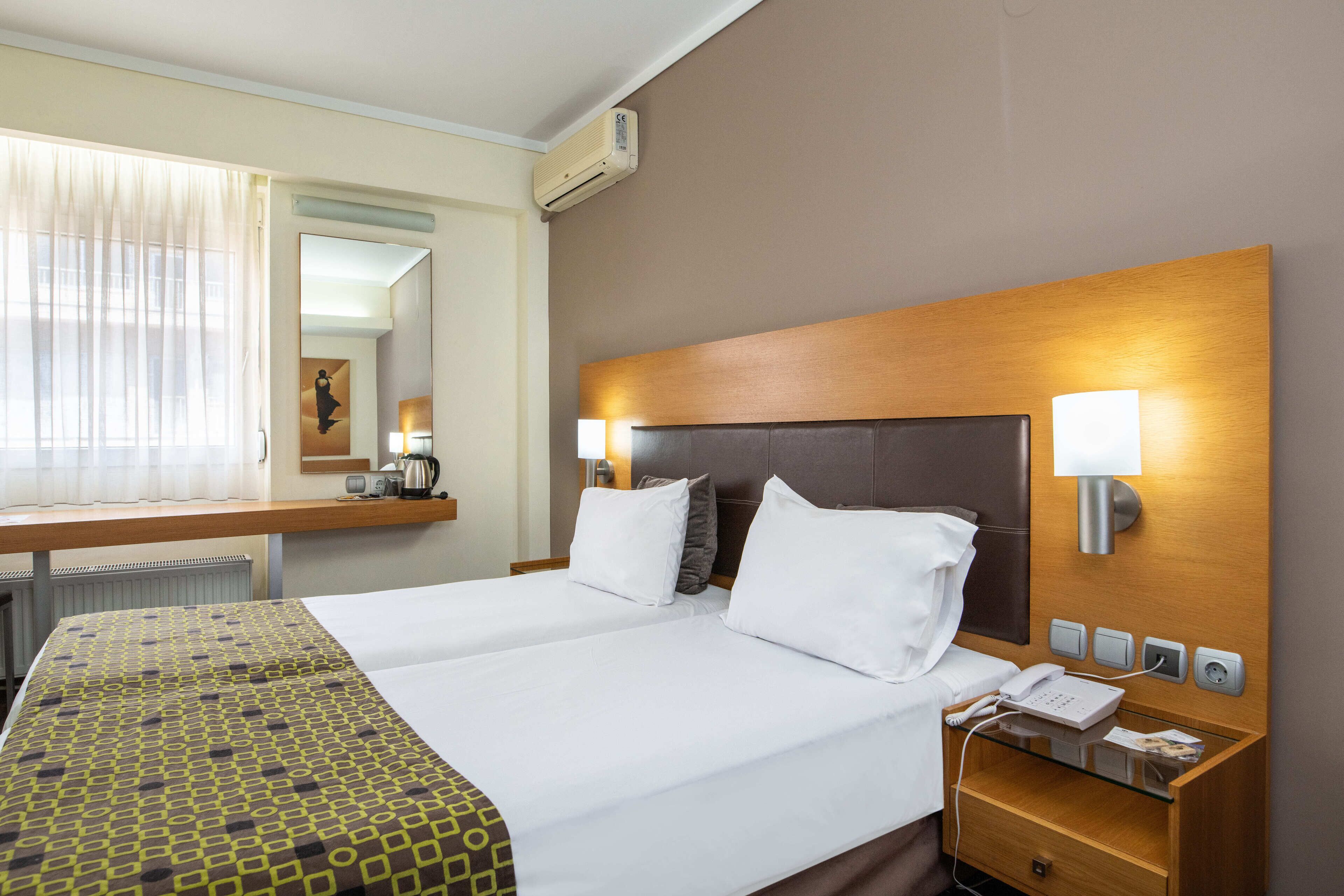 Una habitación de hotel con una cama grande, mesitas de noche, un espejo y un equipo de aire acondicionado.