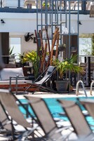 Uma área à beira da piscina com espreguiçadeiras, uma piscina pequena e plantas em vasos.