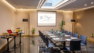 A conference room with a long table, chairs, and a projector screen displaying "The Mayor Hotel" name.