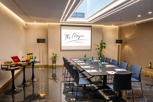 A conference room with a long table, chairs, and a projector screen displaying "The Mayor Hotel" name.