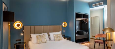 A modern hotel room with a large bed, bedside tables, a wardrobe, and a mirror.
