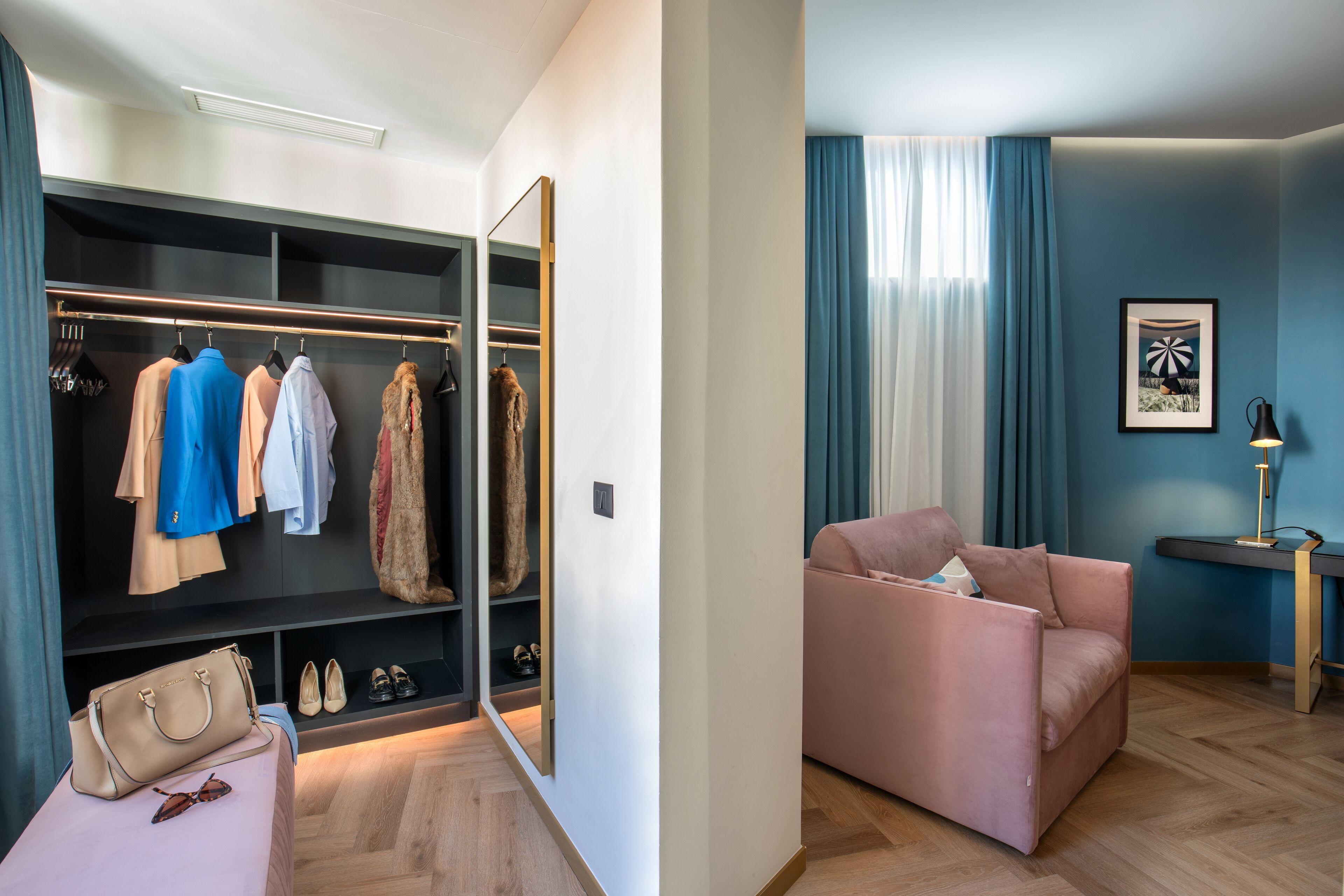 A modern room with a walk-in closet, a pink sofa, and a desk with a lamp.