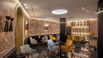 A modern lobby with marble walls, a central seating area with chairs and tables, and a decorative wall panel.