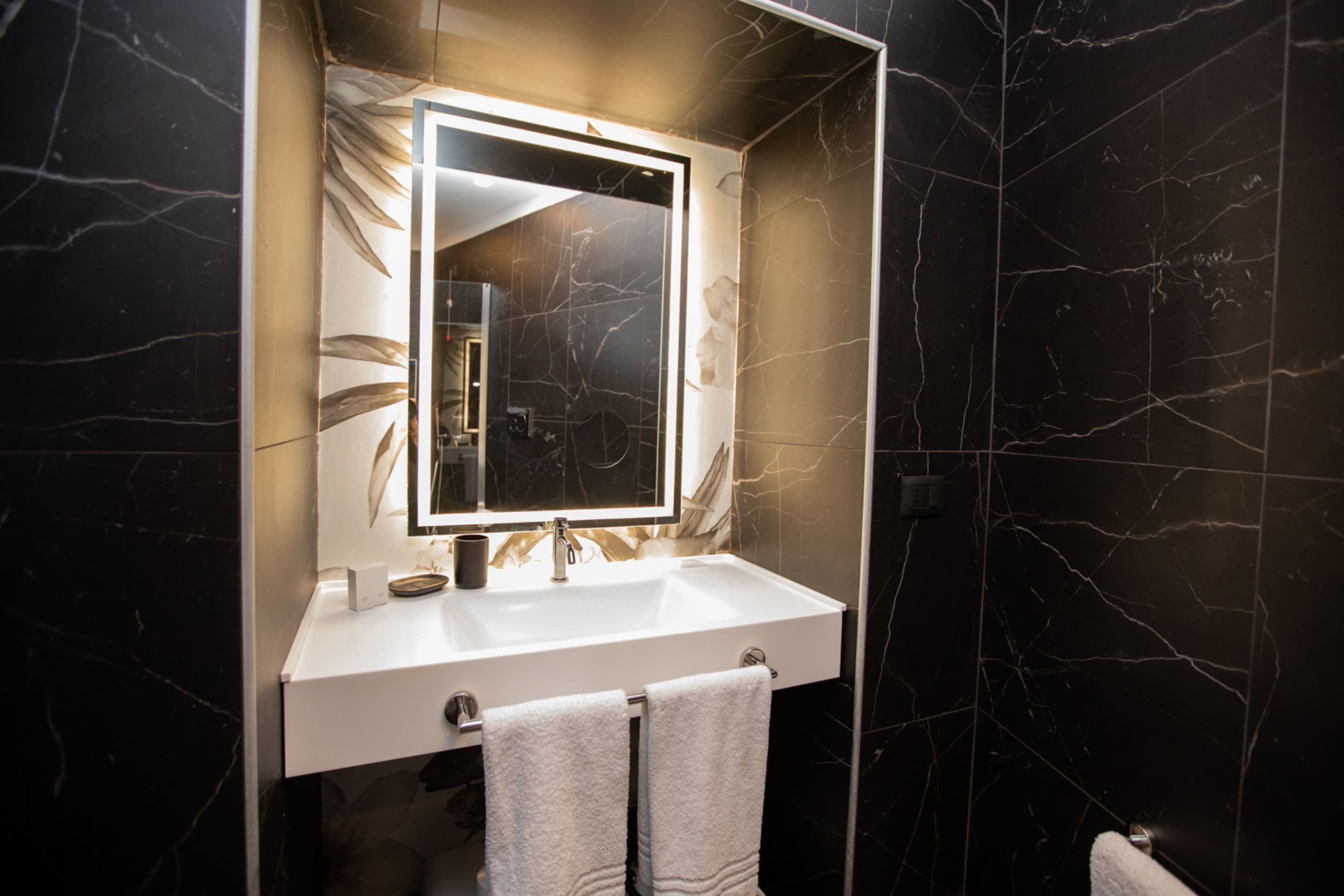 A modern bathroom with a white sink, a large mirror, and black marble walls.