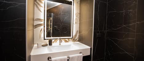 A modern bathroom with a white sink, a large mirror, and black marble walls.